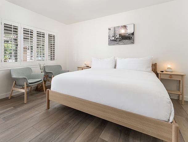 A clean and minimalist guest room with a large bed, two nightstands, and two chairs by the window.
