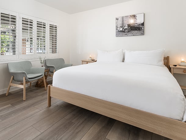 A wide view of a hotel room with a large bed, two chairs, a window, and artwork.