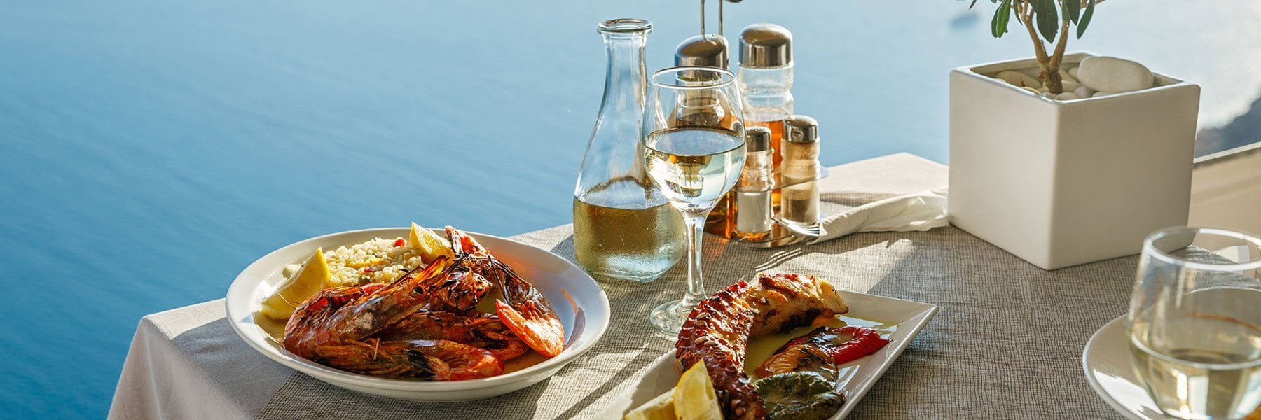 A seafood dish with lobster, rice, and lemon on a table overlooking the ocean.