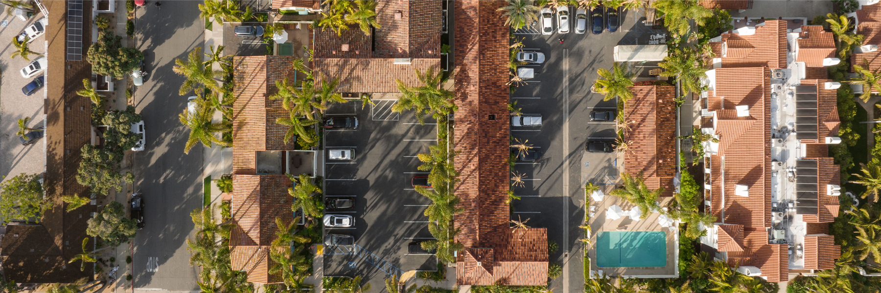An aerial view of the hotel's exterior, showing its parking lot, pool, and terra cotta roofs.