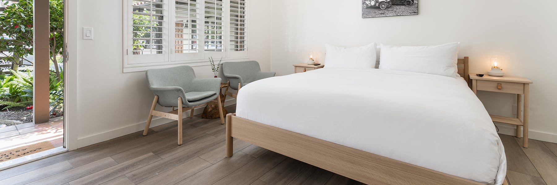 A wide view of a hotel room with a bed, nightstands, chairs, and a window leading to an outdoor area.