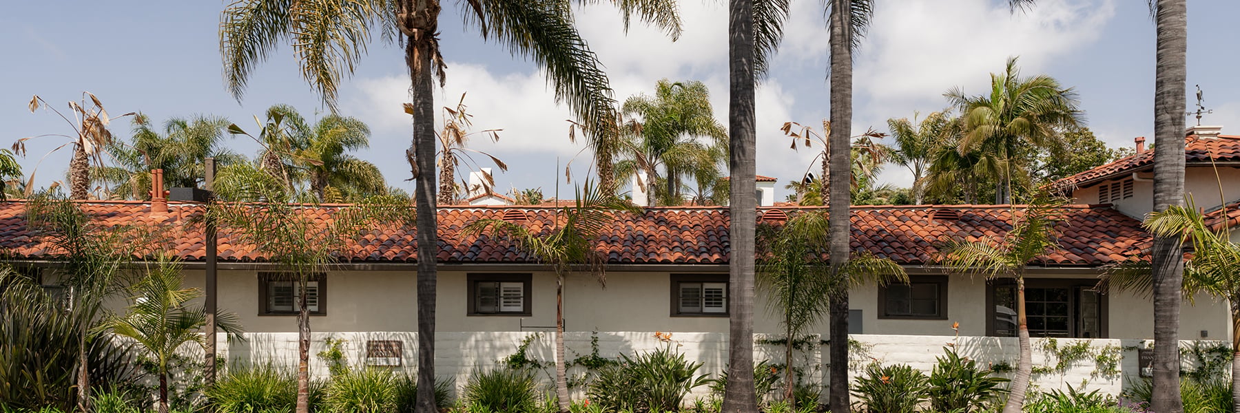 A white stucco building with a terra cotta roof and palm trees in front of it.