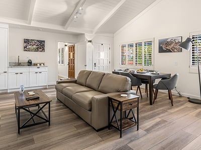 A bright and airy living room with a sofa, coffee table, dining table, and kitchenette.