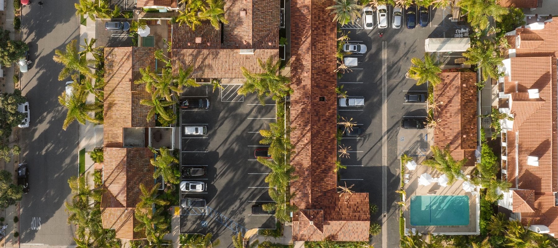 An aerial view of a hotel complex with a parking lot, pool, and palm trees.